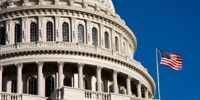American flag waves in the wind next to the dome of the U.S. Capitol
